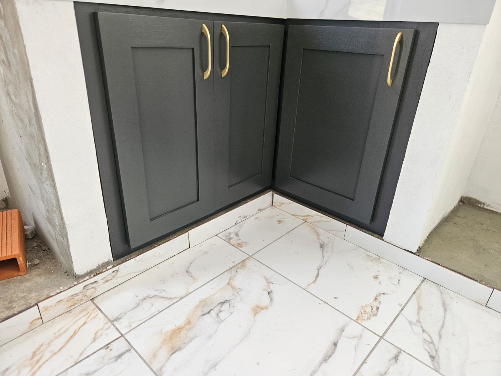 Charcoal shaker base cabinets with brass hardware installed above marble-look floor tiles